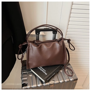 Deep brown pleated hobo bag with knotted handle resting on a silver suitcase