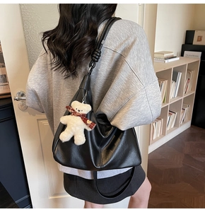 Detailed view of the black leather tote bag featuring a knotted strap and plush bear charm