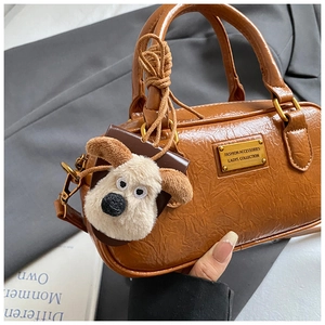 Detail of a brown pleated texture bowling bag with puppy charm and gold metal logo plaque