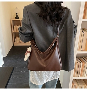 Detail of soft brown leather tote bag with unique knot strap and plush bear charm decor