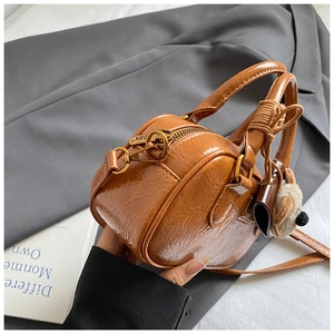 Close-up of brown crinkled leather handbag with metal zipper and plush bear charm