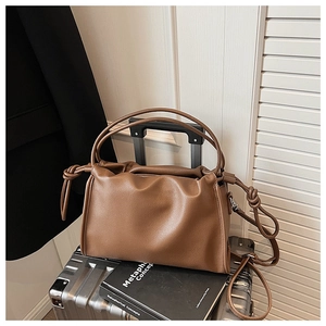 Close-up of brown pleated shoulder bag with knotted strap detail on silver suitcase
