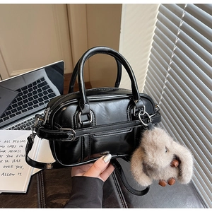 Detail view of a black leather handbag featuring a cute plush bunny charm and silver hardware