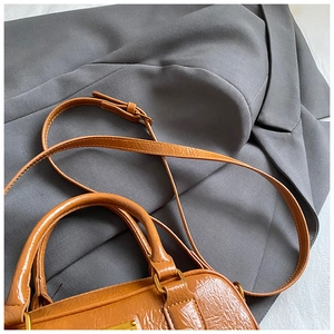 Detail of vintage caramel brown bowling bag with wrinkled leather texture on gray blazer
