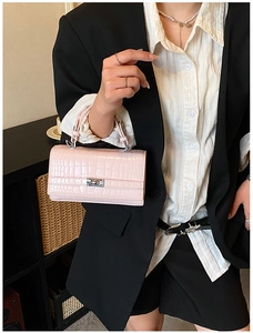 Detail of light pink crocodile pattern handbag with silver clasp held by a model