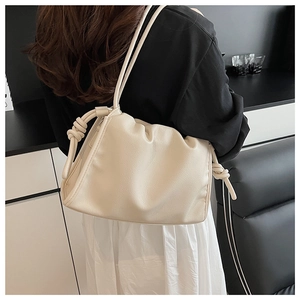 Detail of a creamy white pleated shoulder bag with knot strap on a model shoulder