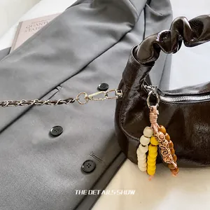 Close-up of dark brown glossy chain bag with pleated handle and colorful bead charm