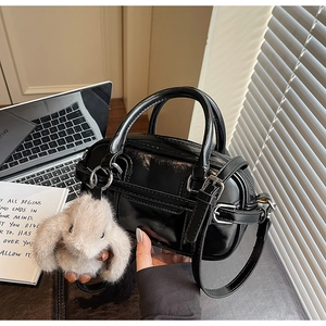 Close-up of black glossy patent leather handbag featuring a fluffy rabbit charm detail