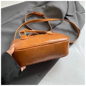 Detailed macro view of caramel waxed leather texture and metal logo on a vintage shoulder bag