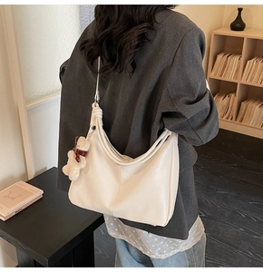 Detail of a large cream crescent shoulder bag with a cute plush bear charm on PU leather