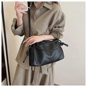 Detail of black pebbled leather texture and side knot design on a pleated shoulder bag