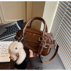 Detail of a brown leather Boston bag with a plush charm and adjustable shoulder strap