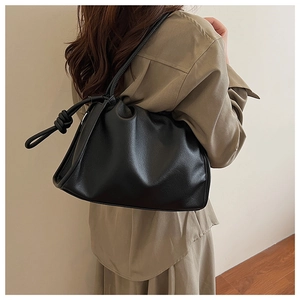 Detail view of black pleated leather underarm bag with knot strap on a model