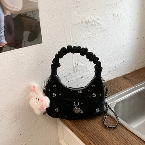 Détail du sac hobo en daim noir avec broderie florale, nœud et breloque lapin en peluche
