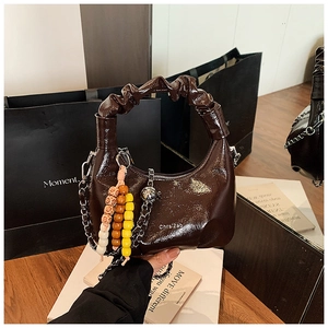 Detail of dark brown patent leather handbag with pleated handle and beaded charm accessory