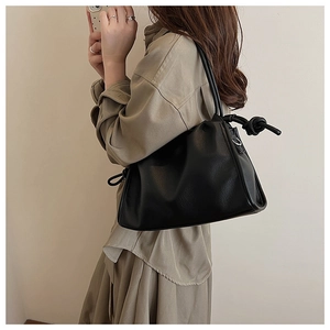 Detail showing knotted strap connection and pebble texture of a black shoulder bag