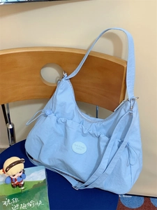 Détail d'un sac hobo bleu ciel avec patch logo rond, posé sur une chaise en bois naturel