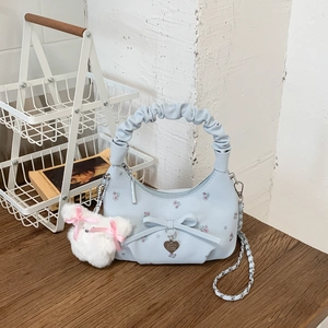 Détail d'un sac à main bleu clair fleuri avec nœud, pendentif cœur et ours en peluche