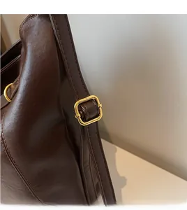 Detail of adjustable deep brown faux leather shoulder strap with gold metal buckle hardware