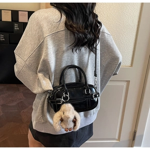Close-up of a black glossy crossbody bag with a cute beige bunny plush pendant detail