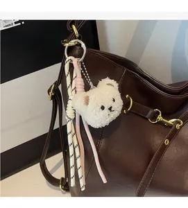 Close-up of a plush bear bag charm with embroidery and braided rope on a leather bag