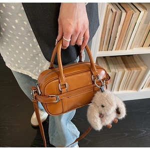 Detail of small brown Boston bag with decorative strap and plush bunny charm accessory