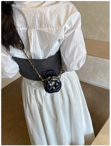Détail d'un mini sac rond en cuir matelassé avec boucle fleur dorée sur un mannequin