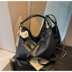 Detail view of large black tote bag with gold metal buckle and white plush bear charm