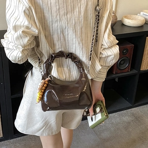 Brown patent leather pleated handbag featuring silver chain strap and beaded charm