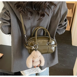 Macro view of olive green patent leather handbag featuring belt buckle and plush bunny charm