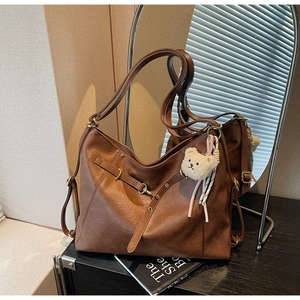 Detail of a large brown tote bag featuring gold metal buckles and a cute teddy bear charm
