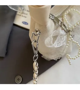 Close-up of beige pleated bag featuring lace trim, pearl pendant, and silver chain strap