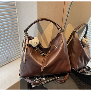 Detail view of large dark brown leather tote bag with plush bear charm and woven tassel