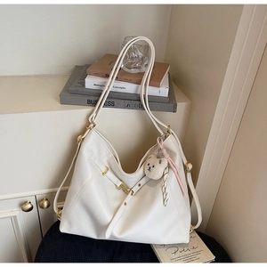Close-up of white hobo bag featuring litchi grain texture and a plush bear pendant