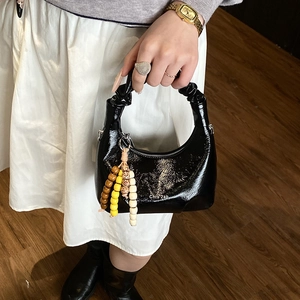 Detail of glossy black crescent handbag featuring pleated handle and beaded charm accessory