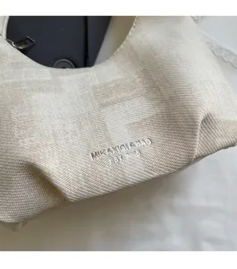 Close-up of cream textured fabric with F-letter jacquard and silver logo on the handbag