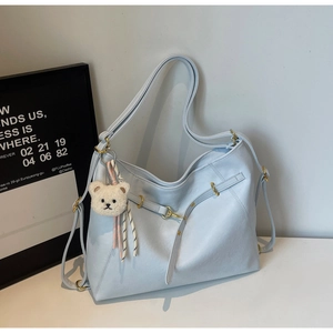 Close-up of light blue leather tote bag with gold hardware and white plush bear charm