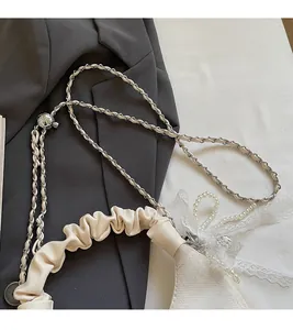 Close-up of cream pleated handbag with leather chain strap and decorative lace bow detail
