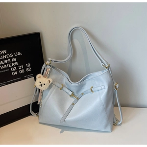 Detail of light blue leather tote bag with gold hardware and plush bear pendant accessory