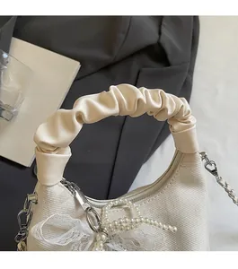 Detail of cream pleated dumpling bag featuring lace trim, pearl pendant and silver chain strap