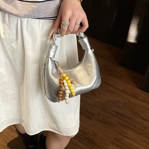 Detail of silver metallic dumpling bag featuring unique knotted handle and colorful bead tassel