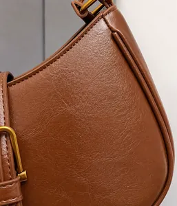 Detail of soft brown pebble leather texture and vintage gold metal buckle on shoulder bag