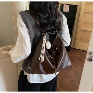 Close-up of vintage dark brown faux leather backpack with tassel and plush pompom charm