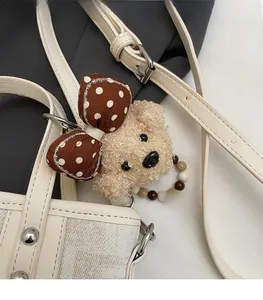 Détail d'un charme ours en peluche avec nœud à pois sur un sac seau texturé
