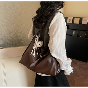 Brown leather tote bag worn by model with bear charm and striped ribbon detail