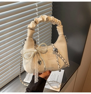Detail of cream pleated handbag with pearl bow lace and silver heart pendant charm
