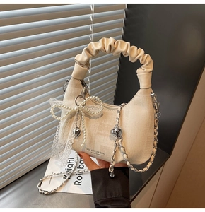 Detail of off-white hobo bag with jacquard texture and pearl bow charm accessory