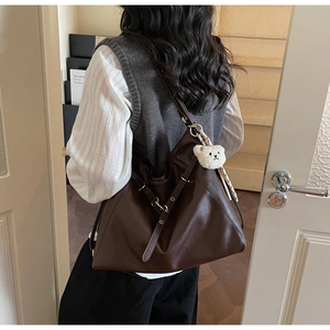 Detail of dark brown tote bag on shoulder with plush bear charm and gold hardware