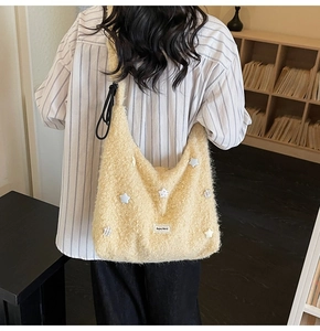 Detail of beige fuzzy hobo bag with star charms and Begou Mersi label on plush fabric