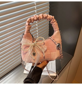 Detailed close-up of pink denim bag with lace bow, pearls and metal heart pendant